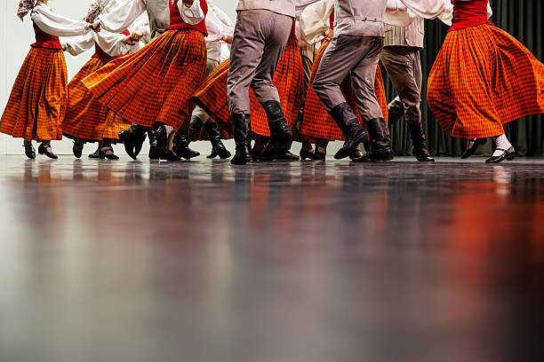 A group of folk dancers performs a lively routine in coordinated traditional costumes, with red vests and flowing orange plaid skirts. Dynamic movement and cultural unity with copy space