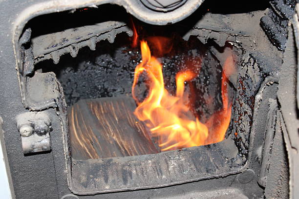 A stove burns wood logs inside. Flames flicker and create heat. The stove shows signs of use with ash and soot around the firebox. This is a common sight during winter nights.