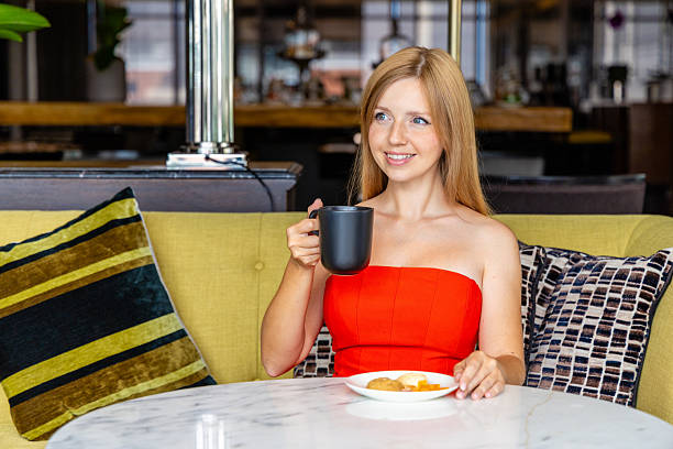 Woman enjoying coffee in modern cafe, wearing red dress, sitting on