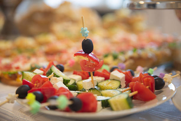 Plate of colorful skewers with tomatoes, cucumbers, feta cheese, and olives at a catering event