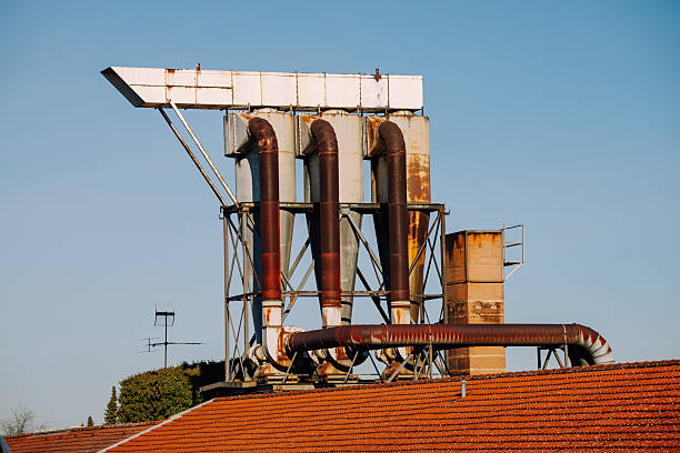 Large industrial ventilation and filtration system with rusted metal pipes installed on a factory rooftop under a clear sky.