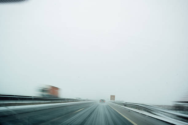 Snow-covered highway with low visibility and vehicles driving ahead during winter weather conditions.