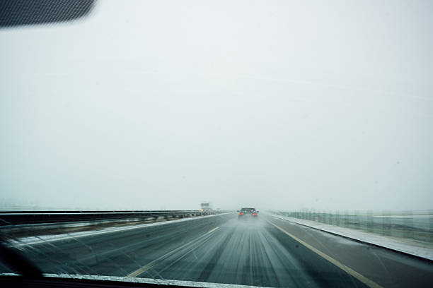 View of a motorway during snowfall with icy road surface and limited visibility, photographed from inside a vehicle.