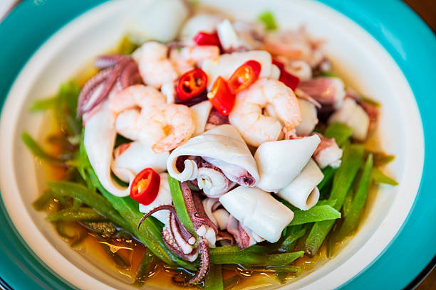 A vibrant dish featuring fresh shrimp, squid rolls, and crunchy green bamboo shoots, garnished with red chili rings for a pop of color.