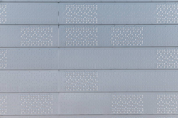 Oslo, Norway - Winter: Close-up view of a contemporary building facade featuring perforated metal panels and repeating horizontal lines. The minimalist architectural detail highlights industrial textures, soft metallic tones and precise geometric patterns, reflecting modern Scandinavian design principles and clean urban aesthetics commonly seen in Oslo’s contemporary architecture