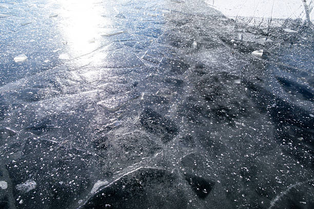 Oslo, Norway - Winter: Close-up view of fractured ice sheets and delicate frozen textures floating on a partially frozen water surface in Oslo. The image highlights natural winter patterns formed by cold temperatures, with crystalline ice fragments, bubbles and snow particles creating an abstract, textured surface that reflects Scandinavian winter conditions and seasonal cold weather