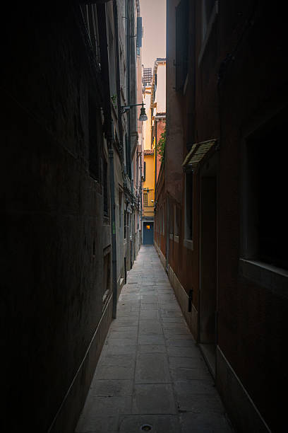 A narrow and quiet alley in Venice, Italy, framed by tall historic buildings and soft natural light filtering from above. The empty stone pathway creates a strong sense of intimacy and depth, revealing the lesser-known side of Venice beyond famous canals and landmarks. The scene evokes silence, contemplation, and timeless urban character, highlighting the city’s unique architecture and human-scale spaces.