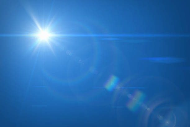 The bright Sun with rays against clear blue sky. Sun is in the upper left corner. There is a sunbeams with natural lens flare. Blue sky and sun flare.