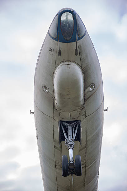 Abandoned vintage aircraft nose and front landing gear viewed from below against cloudy sky