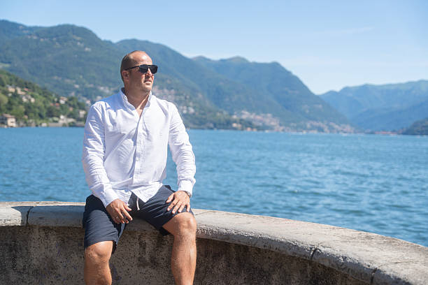 Man sitting by a lake with mountains in the background. Peaceful summer travel scene with nature and water. Concept of vacation, relaxation and freedom.