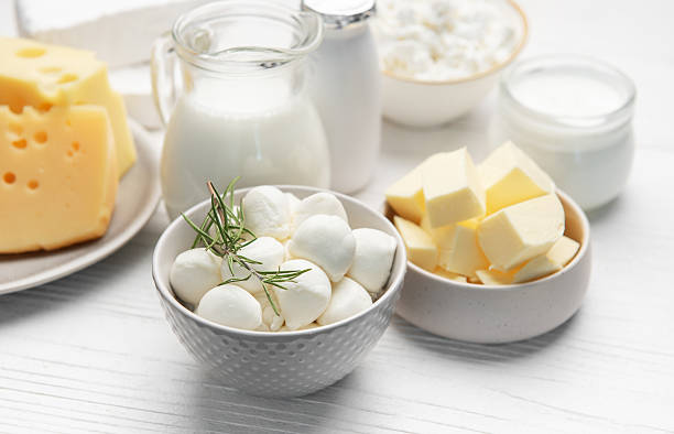 Fresh dairy products like mozzarella, cheddar, milk, butter, and cottage cheese on a white wooden table