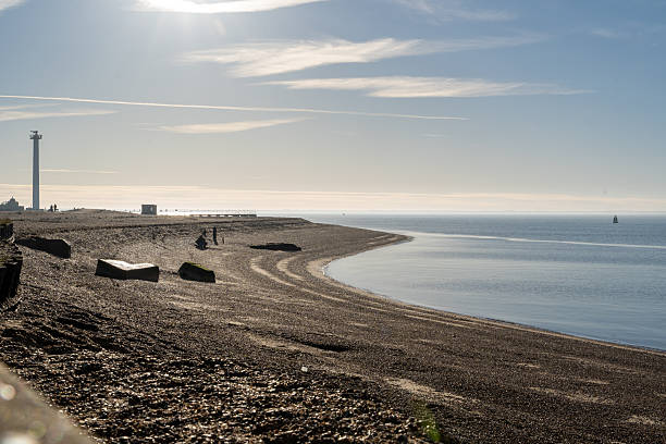 A young black girl stands at the edge of the sea, while her younger sister plays nearby and a women sleeps in the sun on Southend-on-Sea beach, Essex, UK.