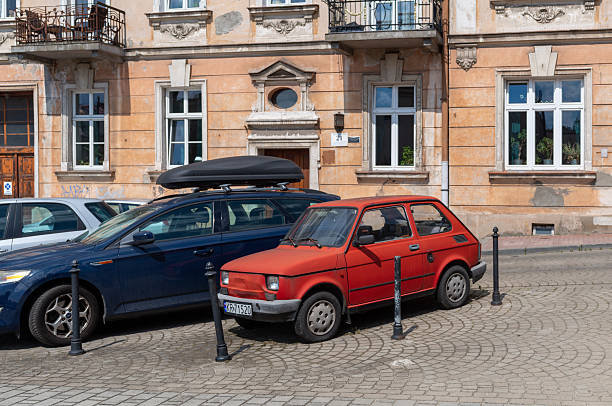 Krakow, Poland – June 29, 2025: Two parked cars stand along a cobblestone street in front of a historic residential building with balconies and weathered facade, showing everyday urban life and architecture in the city center.