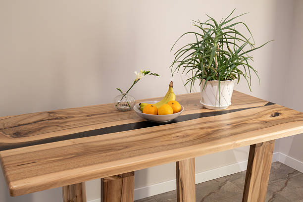 A wooden table holds a bowl of fruit and a plant in a pot in a home space during daytime