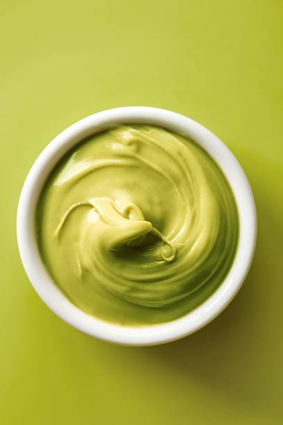 Pistachio cream spread in a white bowl on a green background. Green color. Top view