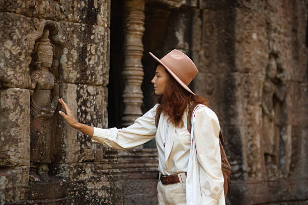 Angkor Wat Ta Som Temple Travel scene: Asian woman tourist in hat touching Khmer stone reliefs at ancient ruin in Cambodia, high quality conceptual image for tourism, history, culture, advertisement and editorial use.