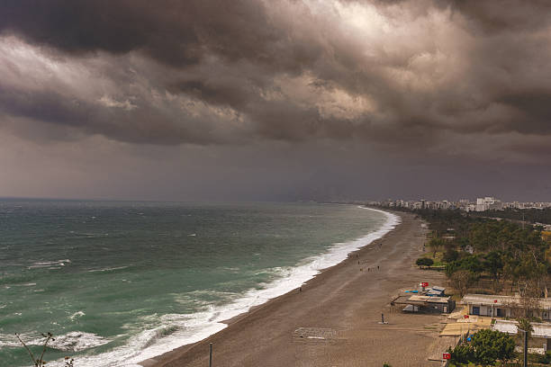 A high-angle view of Konyaaltı beach in Antalya during a storm and winter season. Storm clouds and the choppy Mediterranean Sea create a dramatic atmosphere.