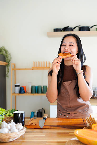 Beautiful young Asian woman with coffee and tasty toasts in kitchen
