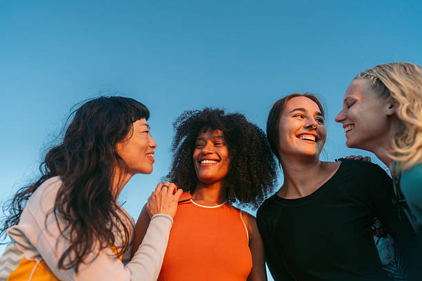 Photo of a multiracial group of female friends, hanging on the beach in their wetsuits, after an active day of surfing