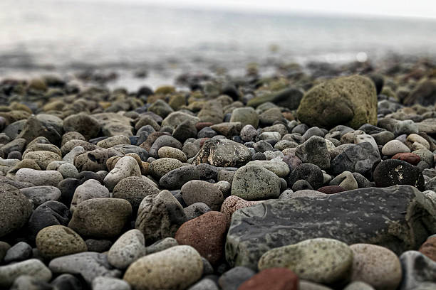 Pebbles and stones lie along a gently rippling shore, their wet surfaces glistening in soft light. A tranquil seascape that evokes calm, nature, and quiet moments by the water.