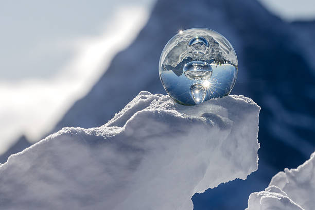A glass ball is positioned on snow in a mountain landscape