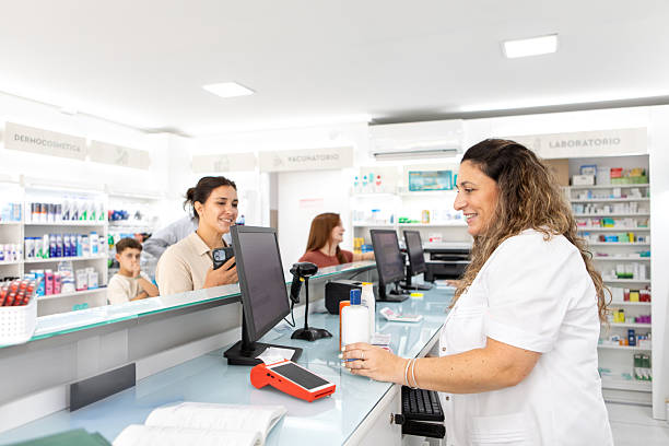 Female pharmacists serving and collecting payments from customers at the pharmacy counter - Buenos Aires - Argentina
