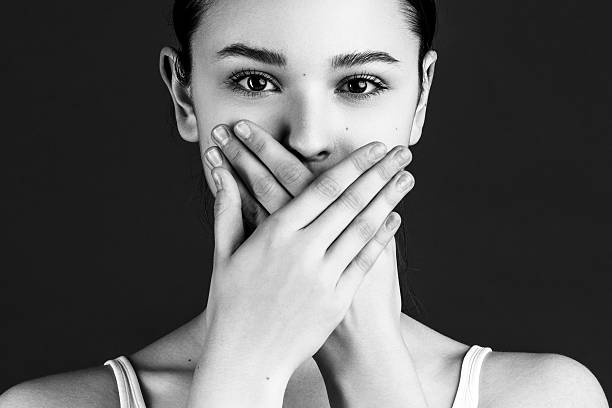 Woman covering mouth with hands, symbolizing silence, secrecy, and suppressing speech