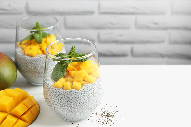 Delicious chia pudding with mango and mint in glasses on white table, closeup. Space for text