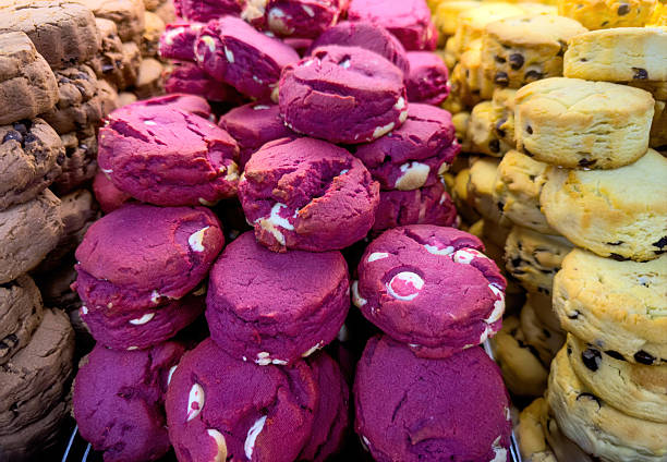 Colorful cookie stacks at a bakery display, close up view of purple, yellow, and chocolate biscuits piled high, vibrant textures