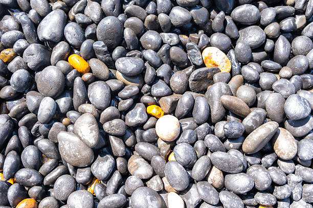 Black pebbles close up background texture, at Mavra Volia beach, Chios island, Greece. Top down view in summer sunshine