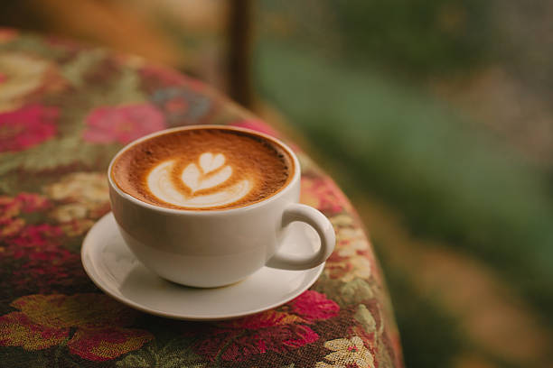 Latte art coffee cup on floral tablecloth with warm cozy atmosphere and blurred background
