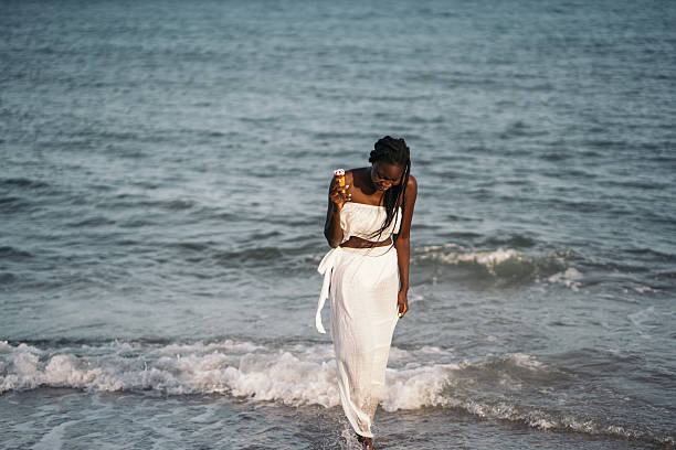 Young woman with braids walking on sunny beach, enjoying ice cream and seaside relaxation