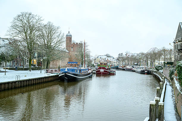 Zwolle snowy Thorbeckegracht during a cold winter morning with houseboats in the canal. The ships, streets and buildings are covered in a layer of snow.