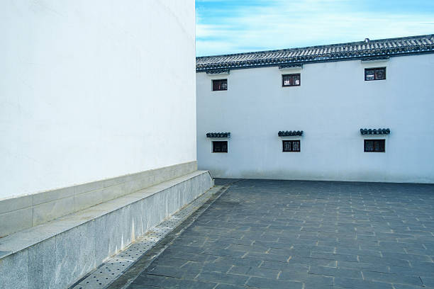 Empty courtyard of a traditional building featuring clean white walls, small windows, and grey stone pavement tiles.