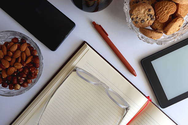 Notebook, pen, tablet, phone, coffee and snacks on white background. Top view.