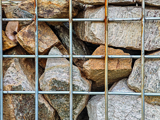 Macro detail texture background of grey stones packed inside a steel wire mesh cage (gabion), construction material.