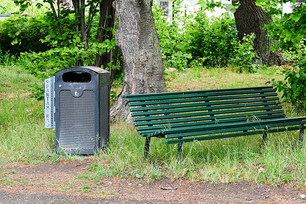 A green park bench sits next to a trash can. The bench is empty