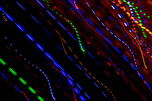 Bright light trails and spots create futuristic patterns against a dark backdrop. Abstract background with defocused lines and spots, made by glowing fiber optic lights.
