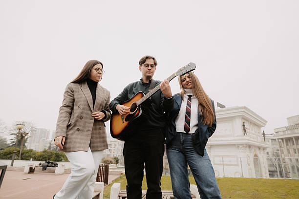 Group of young friends walking together outdoors while one of them plays an acoustic guitar. Concept of friendship, music, youth lifestyle, creativity and urban social life.
