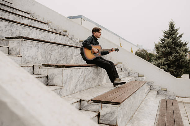 Background of a bearded musician playing the guitar alone in an empty square.
