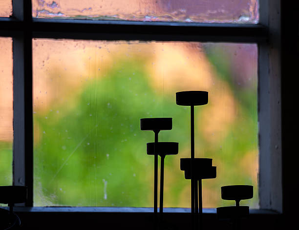 Silhouettes of tall candle holders against a blurred window view.