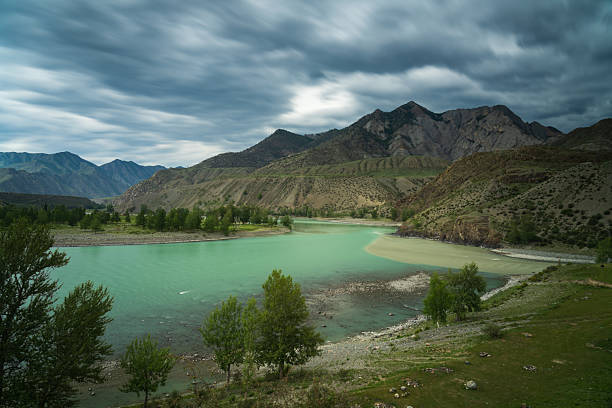 Mountain lake with turquoise water surrounded by hills and forest under dramatic cloudy sky. Suitable for nature, travel, and environmental themes.