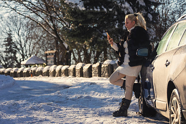 Woman waiting for assistance on a snowy road after car breakdown
