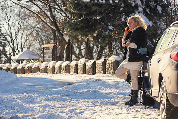 Woman waiting for assistance on a snowy road after car breakdown