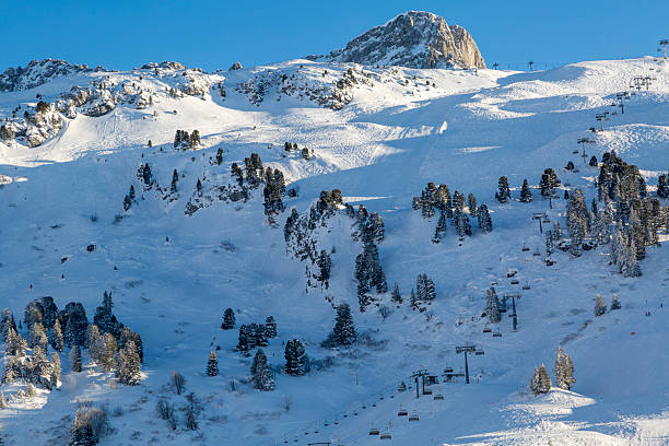 Ski resort with downhill slopes with skiers, chairlift, and snow covered trees in the beautiful Austrian Alps on a sunny day.