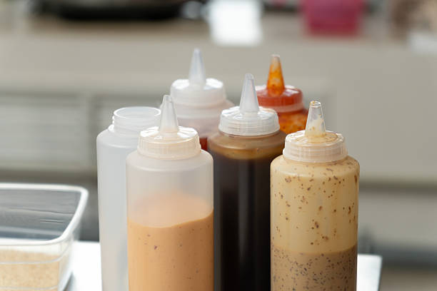Assorted squeeze bottles filled with different sushi sauces standing on kitchen counter in professional restaurant, ready for cooking and serving.