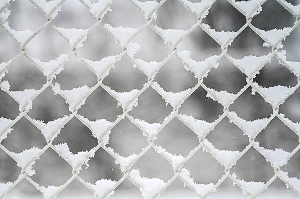 Close up of a metal chain link fence pattern accumulating snow during cold weather