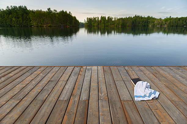woman resting on wooden pier over calm lake with trees and rural houses in background, concept of relaxation, nature retreat, mindfulness