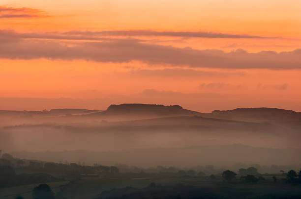 A misty sunrise over rolling hills, with the sky painted in vibrant orange and pink hues.