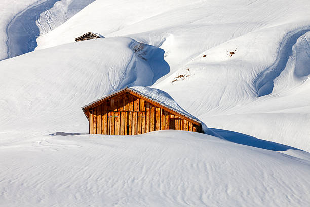 Mountain winter landscape with snow covered wooden shed in Austrian Alps.